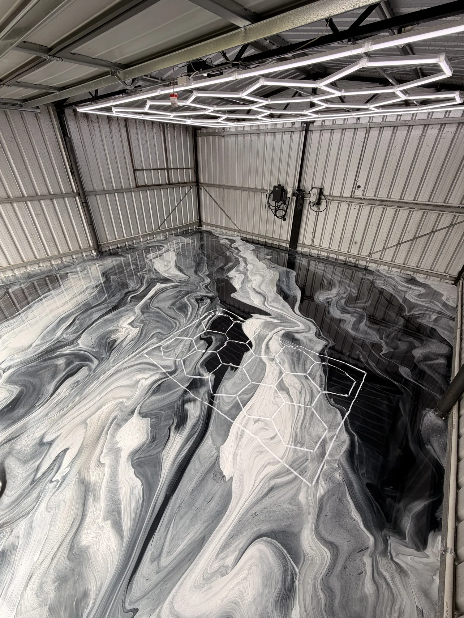 Black, grey and white metallic epoxy floor in a shed under hex lights